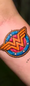 Embroidery style patch tattoo of the Wonder Woman logo on an arm, showcasing 3D thread effects and vibrant colors.