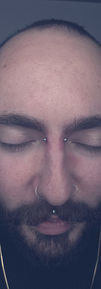 Multiple facial piercings on a man, including a bridge piercing, eyebrow piercing, and a silver septum ring.