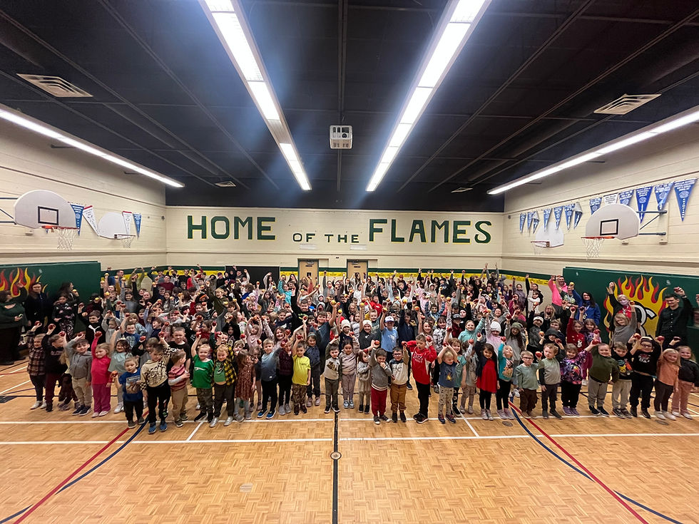 Students of various ages enthusiastically take part in the Great Big Crunch inside a school gymnasium. They bite into apples at the same time, surrounded by colourful posters and supportive educators.