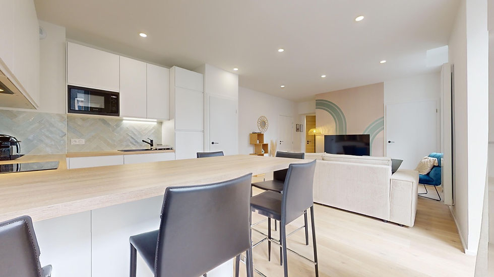 Cuisine ouverte moderne, bar en bois clair, chaises grises élégantes, salon lumineux avec canapé beige et touches de bleu. Colocation Colisée à Annemasse.