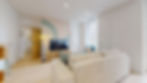 Salon lumineux avec canapé beige clair, coussins bleus et gris, meuble TV en bois clair, télévision à écran plat, fauteuil bleu avec coussin jaune, lampadaire en rotin. Colocation Colisée à Annemasse