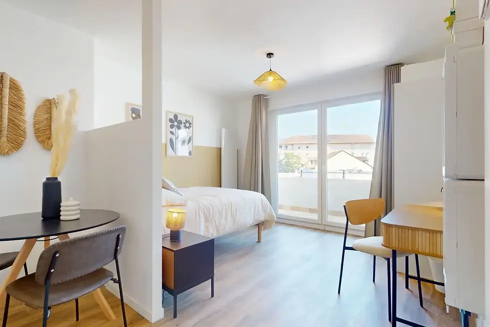  Studio Lazuli à louer à Annemasse, espace lumineux avec lit blanc, coin repas rond, bureau bois et balcon.