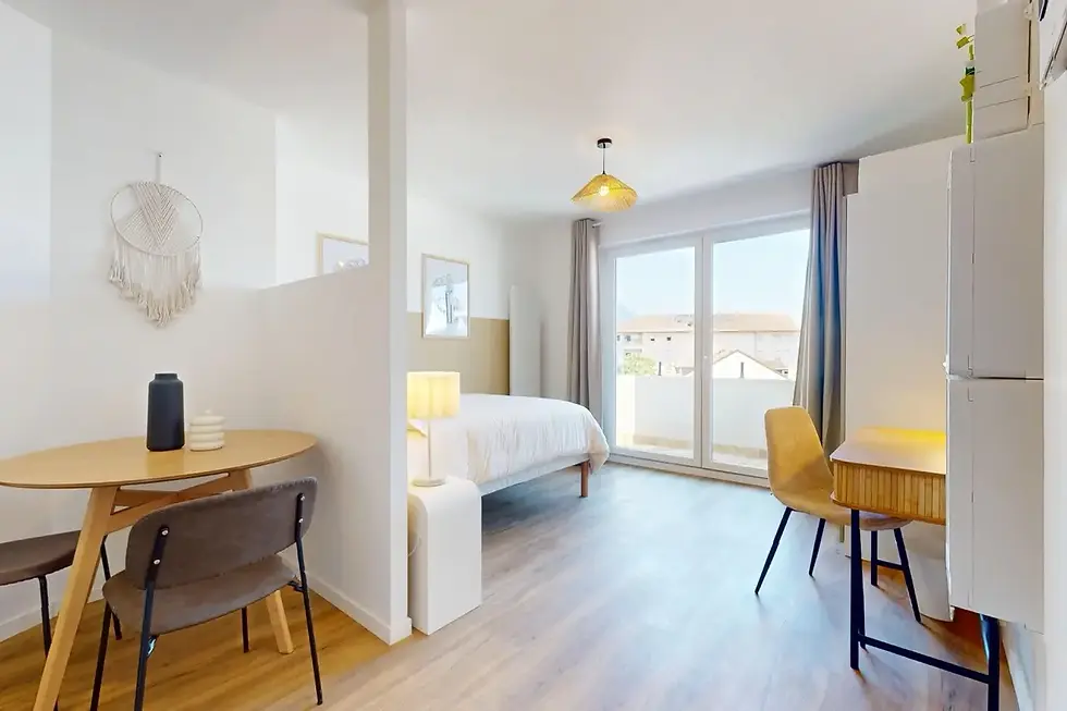 Studio Onyx à louer à Annemasse, intérieur clair avec lit blanc, coin repas bois, bureau et balcon ensoleillé.