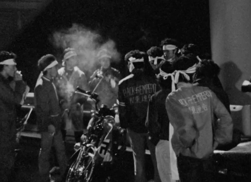 Historical black-and-white photograph of the 'Black Emperor' gang; members are wearing headbands (hachimaki) and jackets with gang lettering while gathered around their machines at night.