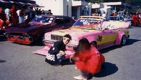 A pink-and-yellow Kaido Racer with a massive front spoiler and widened fenders in a parking lot.