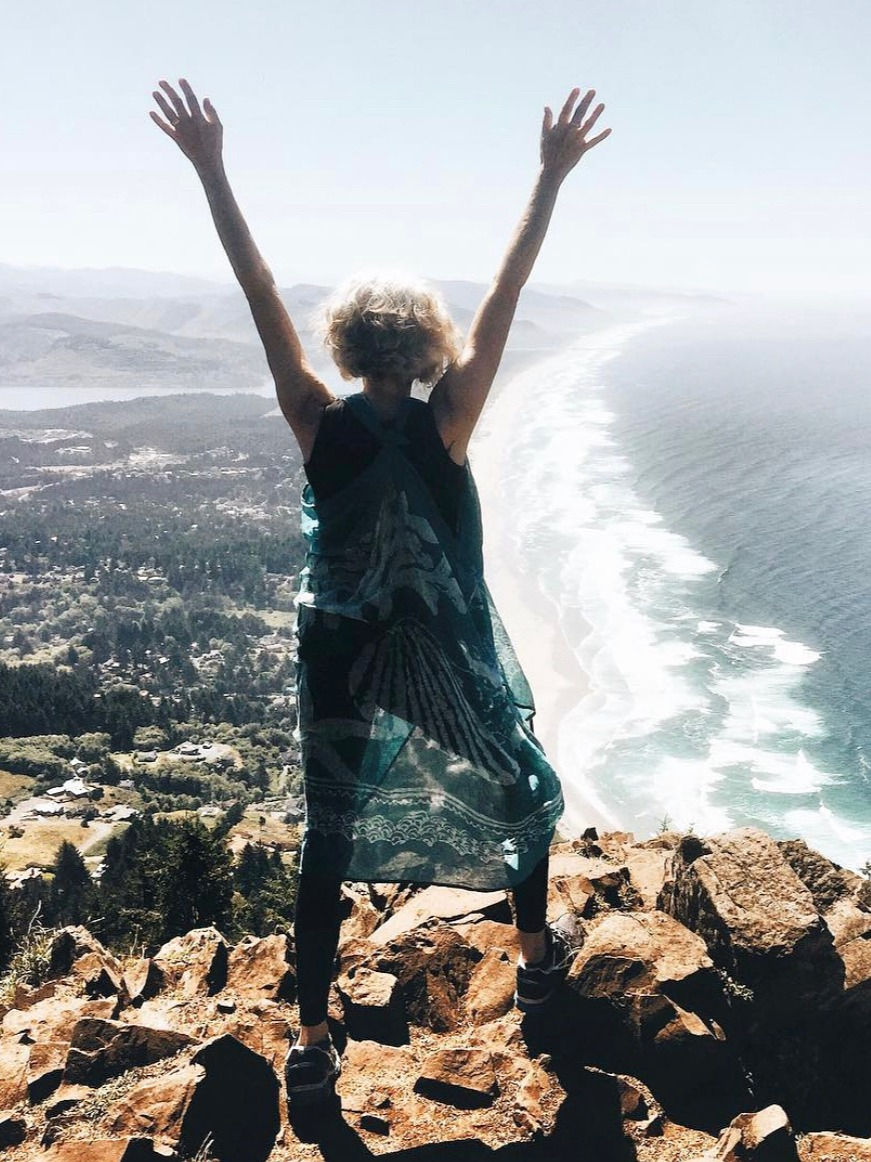 A woman standing on a mountaintop with her hands stretched triumphantly to the sky