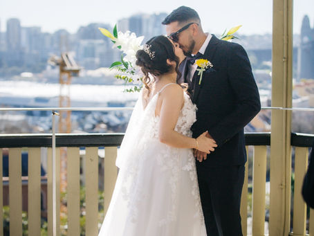 Bride and groom kissing on a harbour-view balcony with the Sydney skyline behind them