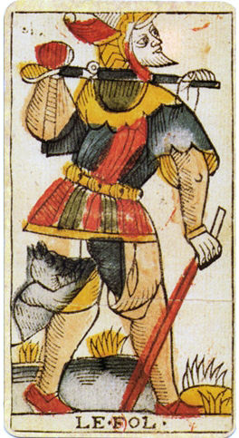 A colorful jester in vivid costume carries a stick over the shoulder. A dog follows him. The card reads "LE FOL." Grass and plants surround them.