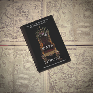 the book One Dark Throne on top of the other books in the series opened to their map pages