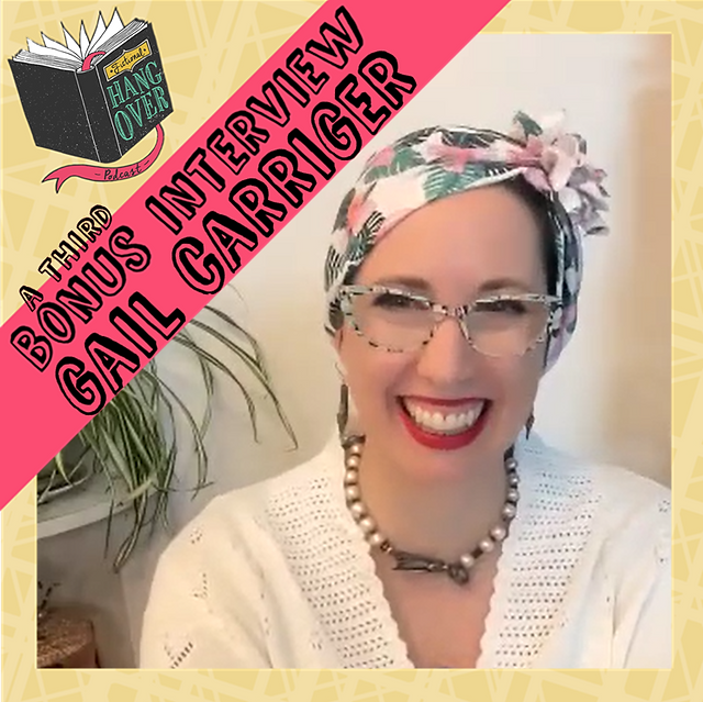 Gail Carriger in a white sweater, glasses, palm tree design turban and red lipstick