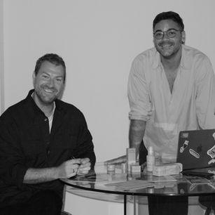 A black and white photo of Egon and Gerard, co-founders of RuMU Beauty, standing at a table with their products.