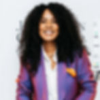 A photo of Char Bailey, a woman with brown skin and long textured hair. She wears a purple suit with a white shirt and an orange pocket square.