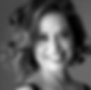 Foto em preto de branco, close de rosto de uma mulher sorridente. Cabelos castanho claros em cachos ondulados na altura do queixo, brincos de argola bem grandes. Fundo cinza. Fim da descrição