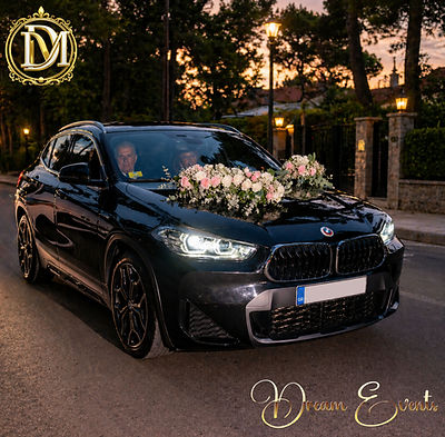 Μαύρη BMW με πολυτελή ανθοστολισμό γάμου και λουλούδια στο καπό κατά τη δύση του ηλίου