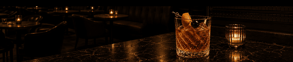 Old Fashioned cocktail garnished with an orange and cherry on a marble bar, surrounded by the warm glow of candles in The Lay