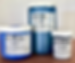 Three jars of Nova Color acrylic paint in Ultramarine Blue, Indianthrone Blue, and Black Pearl on a wooden surface, against a gray wall.