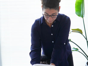 Person in glasses giving myofascial release therapy to someone lying face down. Bright room with white blinds and a green plant in the background.