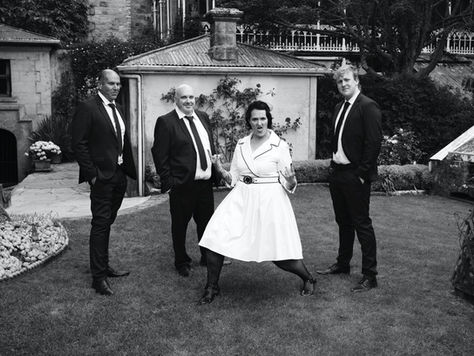 Bride pulling double rock on salute in wedding dress, in garden with groomsmen
