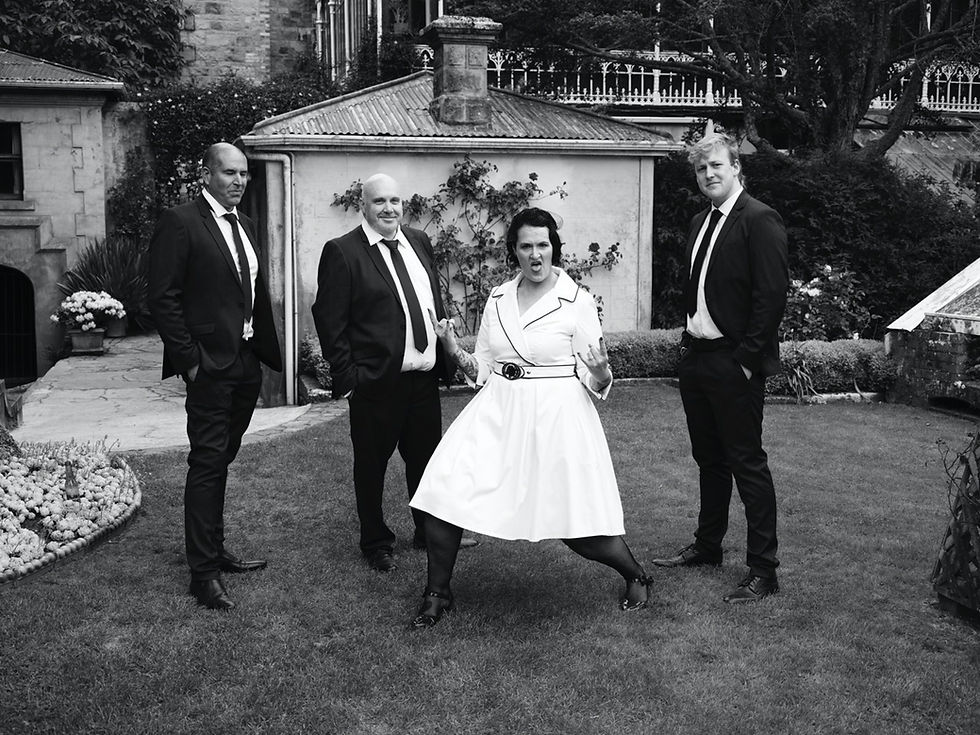Bride pulling double rock on salute in wedding dress, in garden with groomsmen