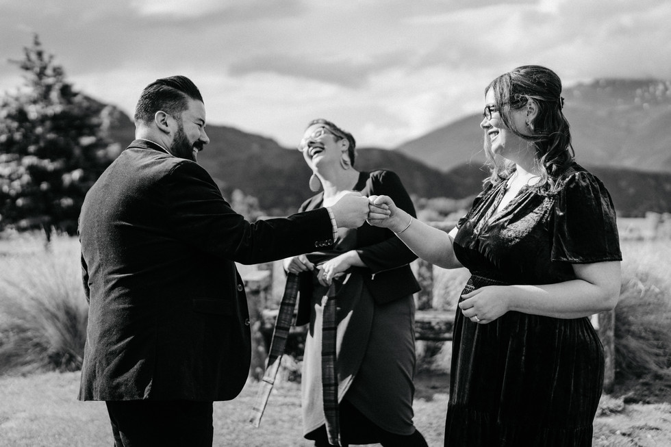 Bride and groom doing their secret handshake during a private garden elopement. Celebrant in background laughing. Glendhu Bay Wanaka NZ