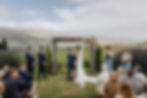 The skies cleared! A rainy day wedding ceremony under a blue sky overlooking vines down to Lake Dunstan and Central Otago Mountains beyond