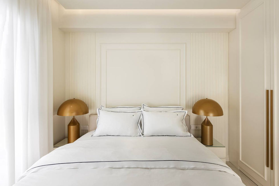 White bedroom with symmetrical golden dome-shaped table lamps and cove ceiling lighting.