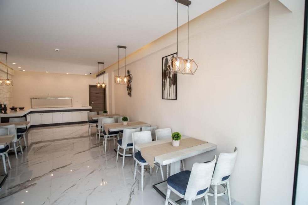 Bright dining room with white marble flooring, light grey chairs, and geometric pendant lights suspended above small square tables.