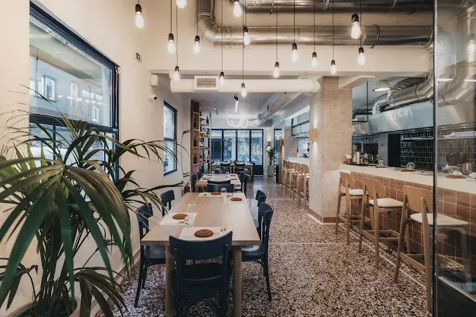 Restaurant dining area with hanging pendant bulbs and exposed ceiling ducts.