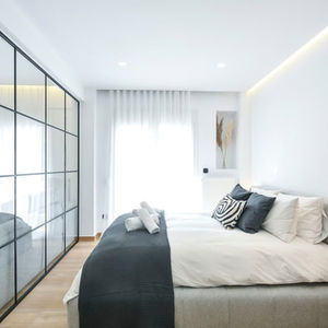 Bright bedroom with natural light filtered through sheer curtains, complemented by ceiling cove lighting and slim vertical pendant lamp.