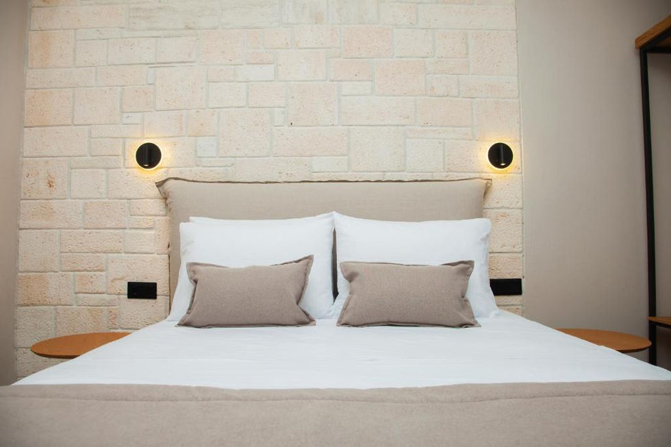 Hotel bedroom with upholstered headboard, stone wall, and circular wall sconces providing ambient light.