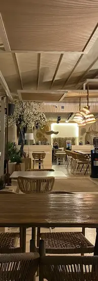 Interior view of a restaurant with wooden tables, rattan chairs, and hanging woven pendant lights creating a warm atmosphere.