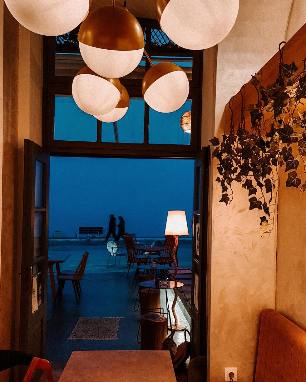 Cluster of spherical pendant lights with gold accents hanging above the café entrance, complemented by a floor lamp casting soft glow onto the terrace.