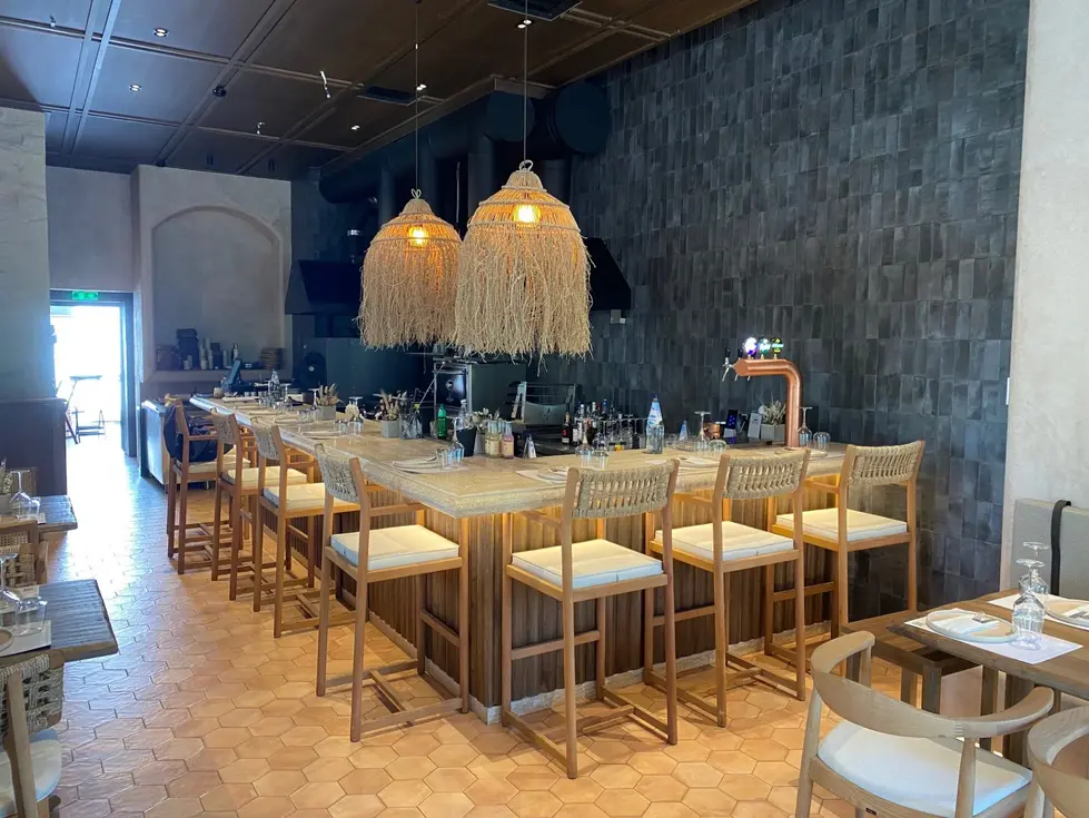 Bar area with high wooden stools, a marble bar top, and oversized woven pendant lamps with fringe details above.