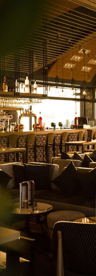 Warm sunset lighting over the bar area of Ciel restaurant in Thessaloniki featuring patterned bar front, pendant lights, and lounge seating.