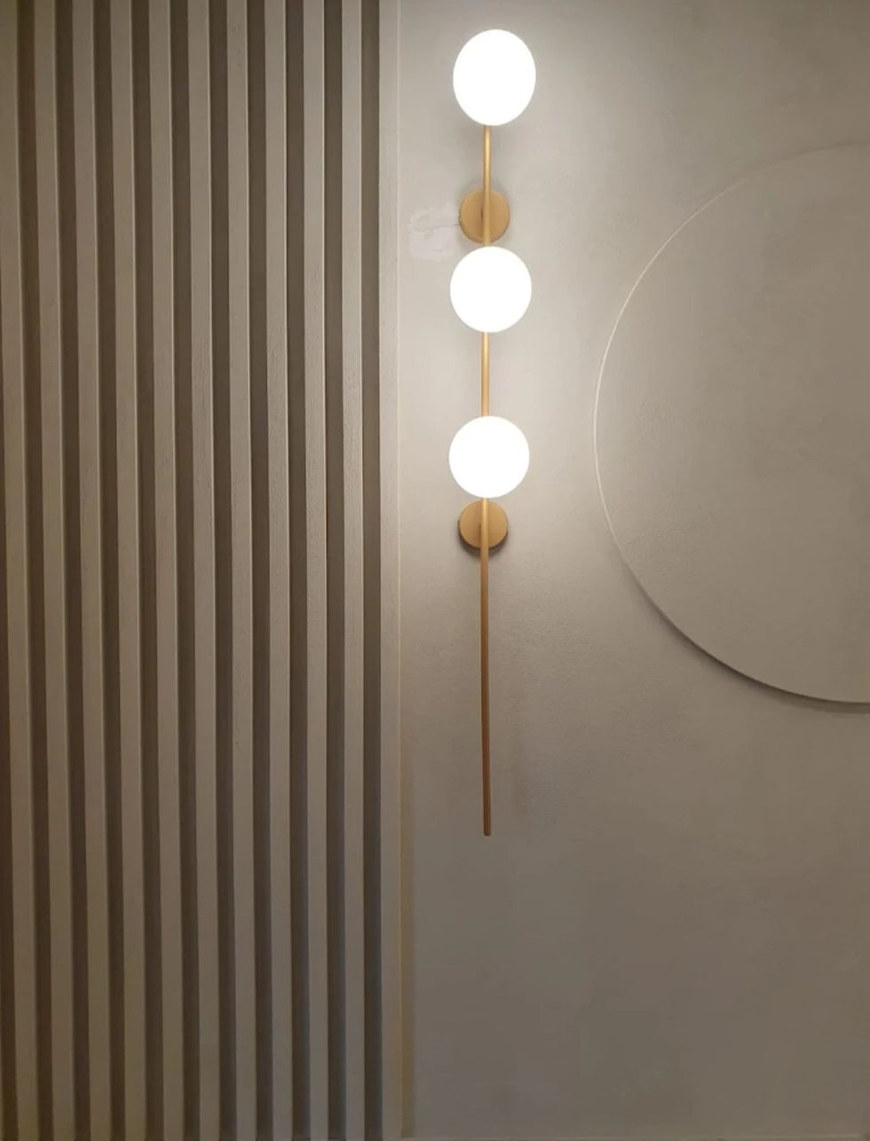 Close-up of decorative wall lamp with three spherical bulbs arranged vertically on a golden support.