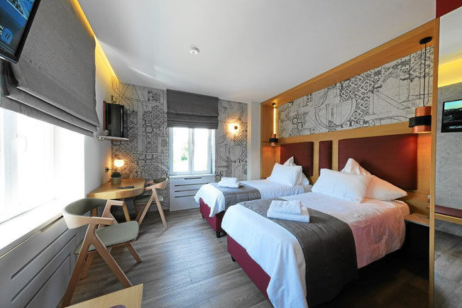 Twin room with map-themed wallpaper – Two beds with upholstered headboards, illuminated by modern wall sconces and soft ambient cove lighting above the feature wall.