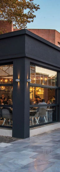 Modern exterior of Plasir Café Patisserie with large glass windows and warm interior lighting visible from outside.