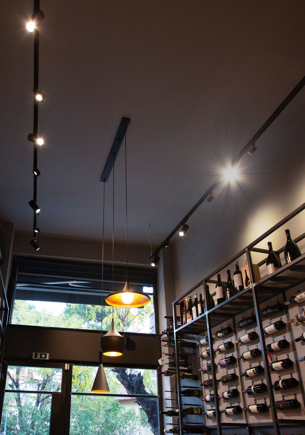 Interior view of wine shop featuring suspended metallic pendants, ceiling track spotlights, and bottle display racks.