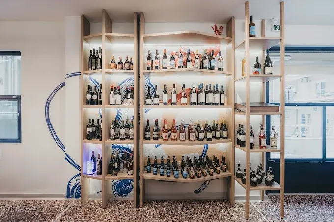 Illuminated wine and spirits display wall with wooden shelving and backlit panels, highlighting the bottles against a mural background in a modern restaurant.