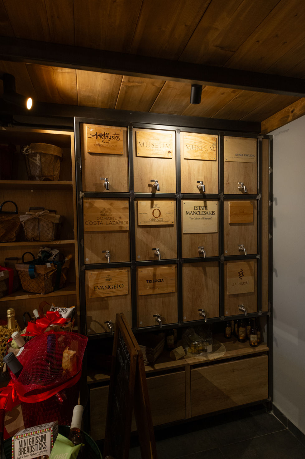Wooden wine tap wall with integrated downlights and shelving baskets illuminated by spotlights.