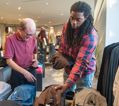 Two men browsing folded shirts and pants in a clothing store.