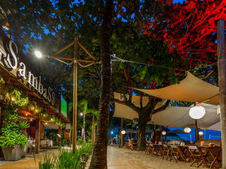 Área de restaurante ao ar livre com mesas postas ao lado da piscina rodeada por plantas tropicais
