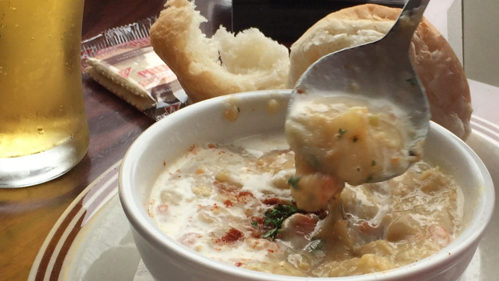 Bol de soupe crémeuse avec cuillère, pain et crackers à côté. Verre de bière en fond. Ambiance chaleureuse, tons dorés et crème.