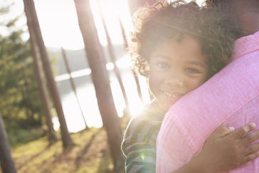 A man and a child embrace warmly in the sunlight, showcasing a moment of affection and joy.