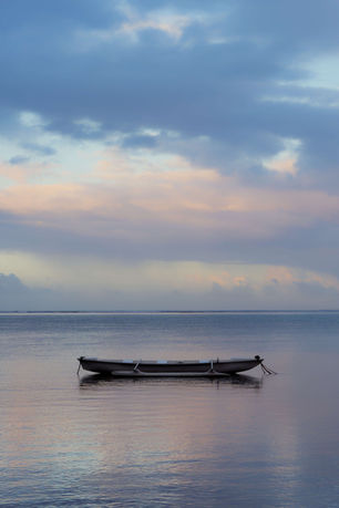Pirogue seule à l'ancre sur une eau lisse, lumière rose et bleue de l'aube