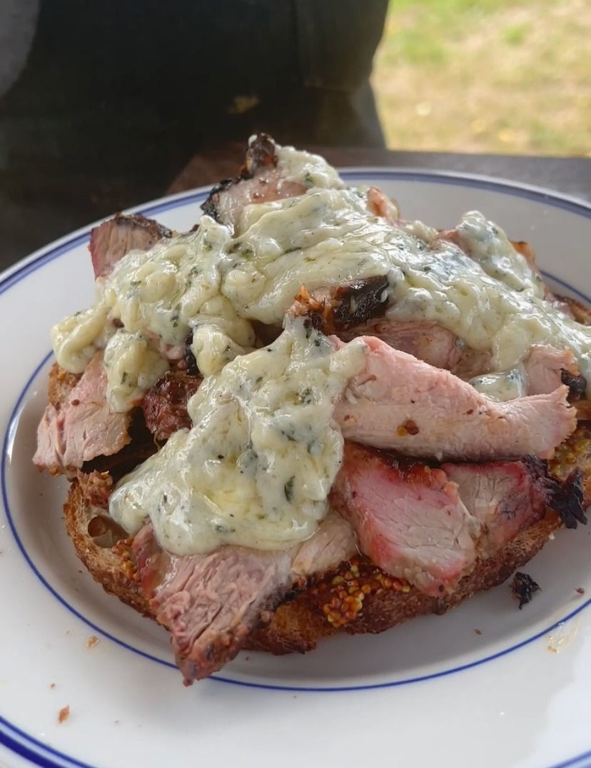 bechamel sauce being poured onto sliced smoked pork loin piled on sourdough bread
