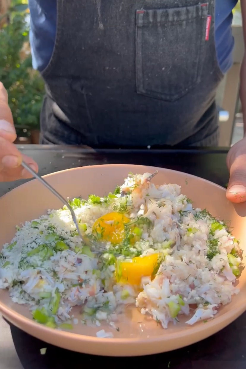 chopped celery, shallot, crab and an egg being mixed together in a bowl