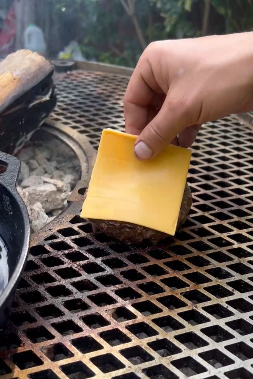American cheese being added on top of the burger on the grill