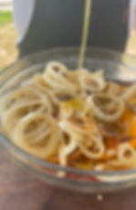 olive oil being poured over grilled onions and grilled peppers in a bowl