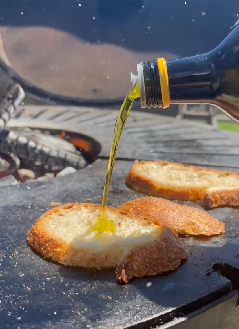 olive oil being poured over slices of sourdough bread on the plancha